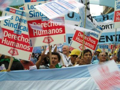 Photograph of protesters in Argentina holding the Argentinian flag and holding signs that read "trade union rights are human rights" in Spanish